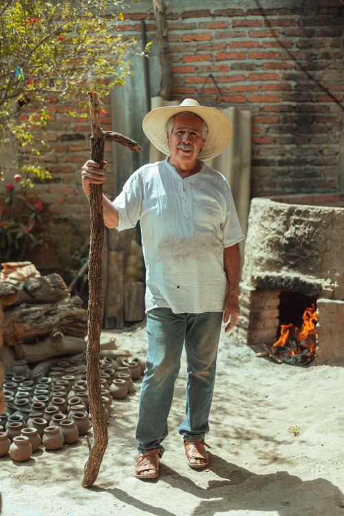 Free Senior man in Mexico holding a rod next to a kiln and ceramic vases outdoors. Stock Photo