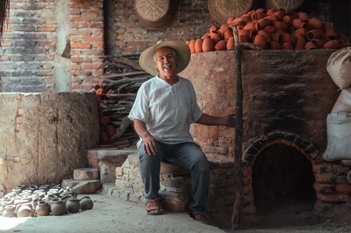 Free Elderly potter in straw hat smiling warmly in a rustic pottery workshop. Stock Photo