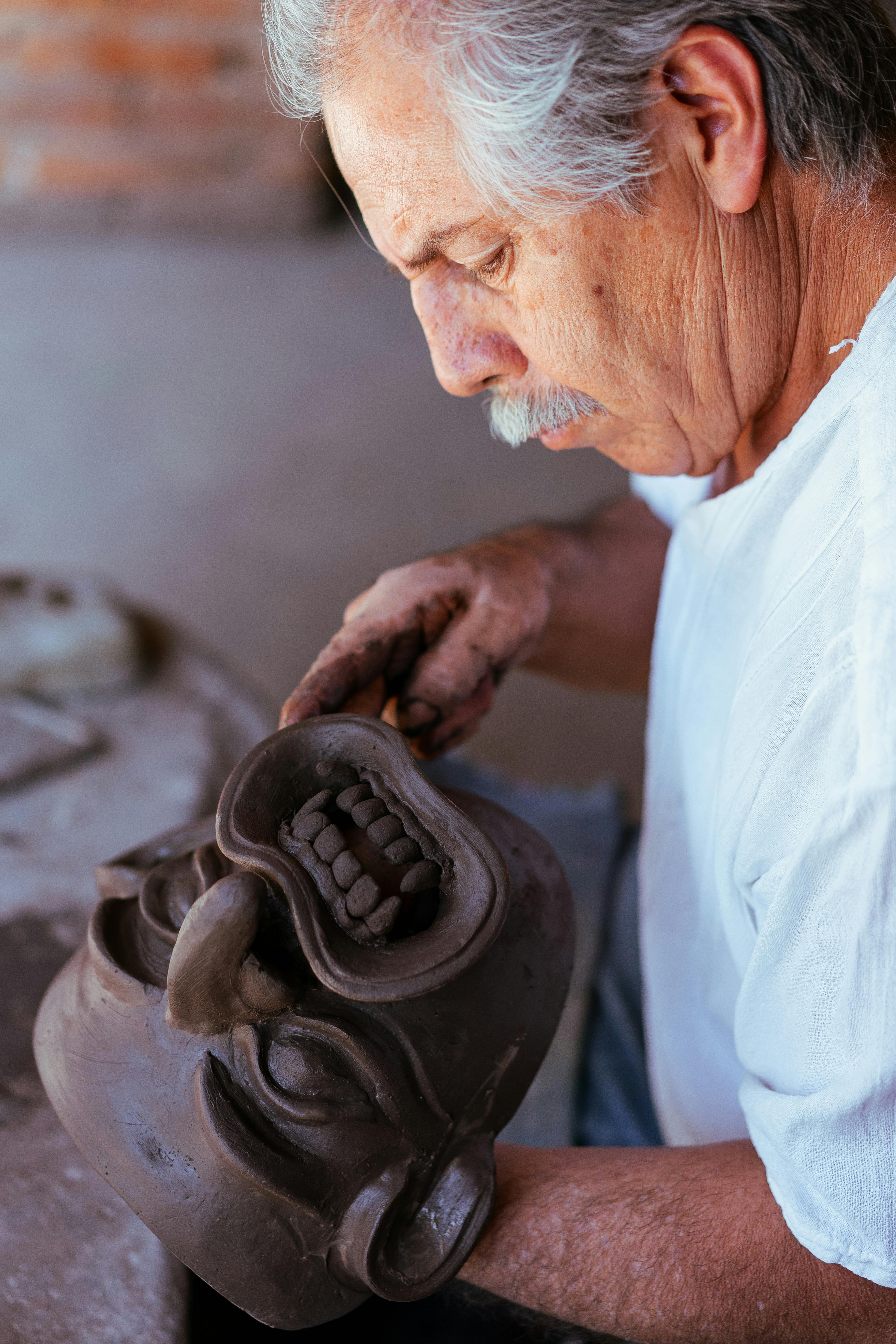Elderly artisan sculpting a traditional clay mask in his workshop, showcasing skilled craftsmanship.