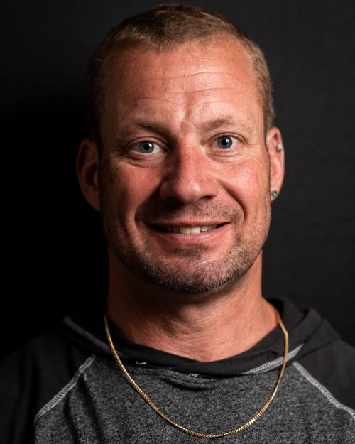Free Close-up portrait of a smiling man wearing a gold necklace and gray shirt against a dark background. Stock Photo