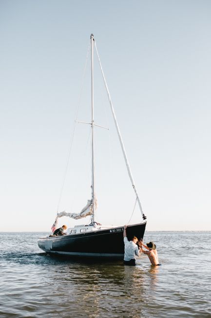 Two people navigating a sailboat in the serene waters of Norfolk, VA, on a sunny day.