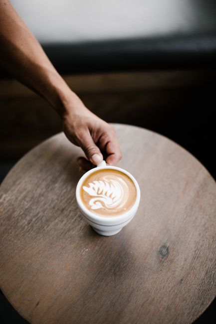 Close-up of a latte with intricate foam art on a wooden table, captured in a cozy cafe setting.