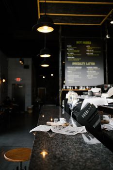 A cozy cafe in Greensboro featuring a granite bar with a cup, newspapers, and hanging lamps.