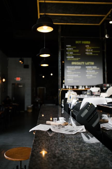 A cozy cafe in Greensboro featuring a granite bar with a cup, newspapers, and hanging lamps.