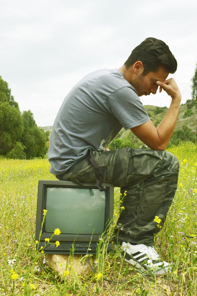 Pensive Man Resting On Retro TV On Lawn