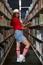 Trendy student in cap with book in corridor of library