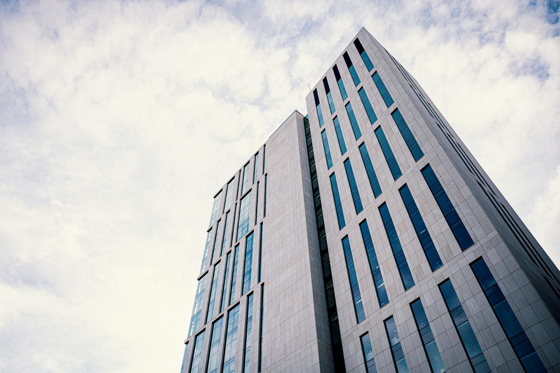 A low-angle view of a contemporary tall office building against a cloudy sky.