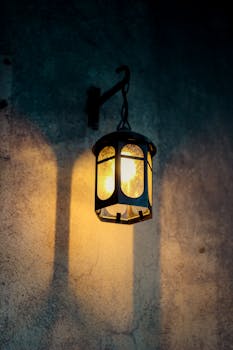 A close-up of a vintage hanging lantern casting warm light on a rustic wall at night.