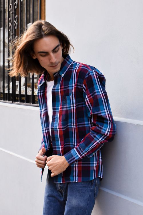 Free Young adult in plaid shirt leaning against wall. Casual urban style. Stock Photo