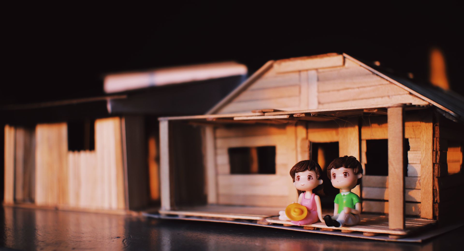 Cute romantic couple figurines with boy and girl placed together on table on toy decorative wooden house with fence in light room