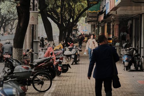 Free Urban scene featuring motorbikes and pedestrians on a tree-lined street with shops. Stock Photo