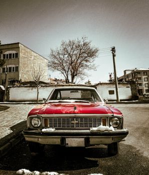 Front view of a vintage red car parked on a snowy street in an urban area.