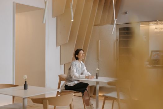 A thoughtful Asian woman sits alone at a modern cafeteria table, evoking a serene and contemplative mood.