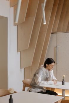 A woman sits in a minimalist café interior, enjoying coffee at a small table. Contemporary and cozy design.