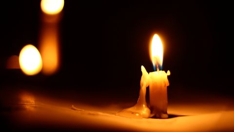 Close-up of a burning candle against a dark background with dripping wax.