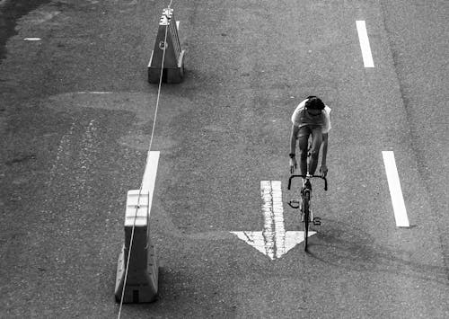 Monochrome Photo of a Person Riding a Bicycle on an Asphalt Road