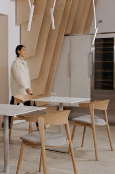 A serene and modern dining space featuring wooden chairs and a blurred figure walking by, highlighting minimalist design.
