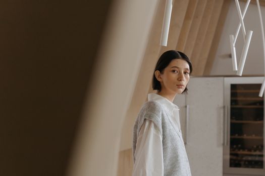 Asian woman with short hair in a Japandi-style café interior wearing a white dress shirt and vest.