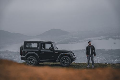 Free A man stands beside an SUV on a hilltop with a scenic view in India. Stock Photo