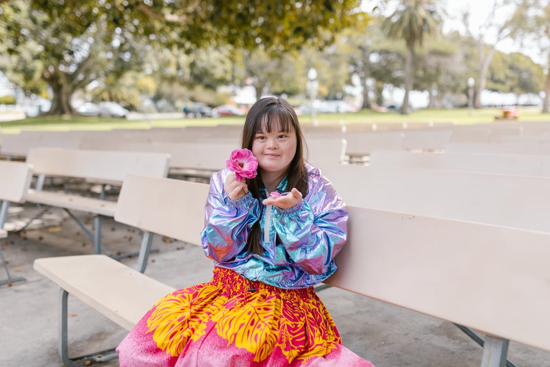 Woman Sitting on Bench while Holding a Pink Flower