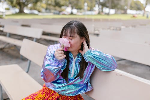 A Girl Smelling a Flower while Sitting on a Bench