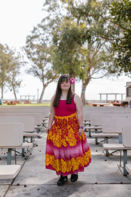 Free Smiling young woman with Down syndrome standing in a park, wearing a vibrant floral dress. Stock Photo