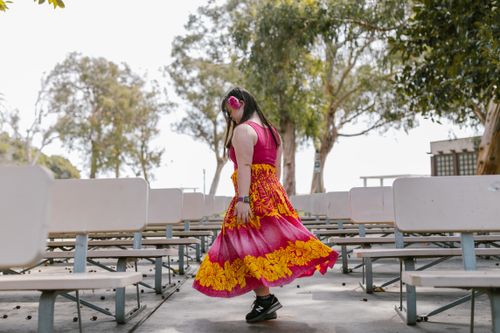 Free A girl in a vibrant floral dress dances among outdoor park benches, surrounded by trees. Stock Photo