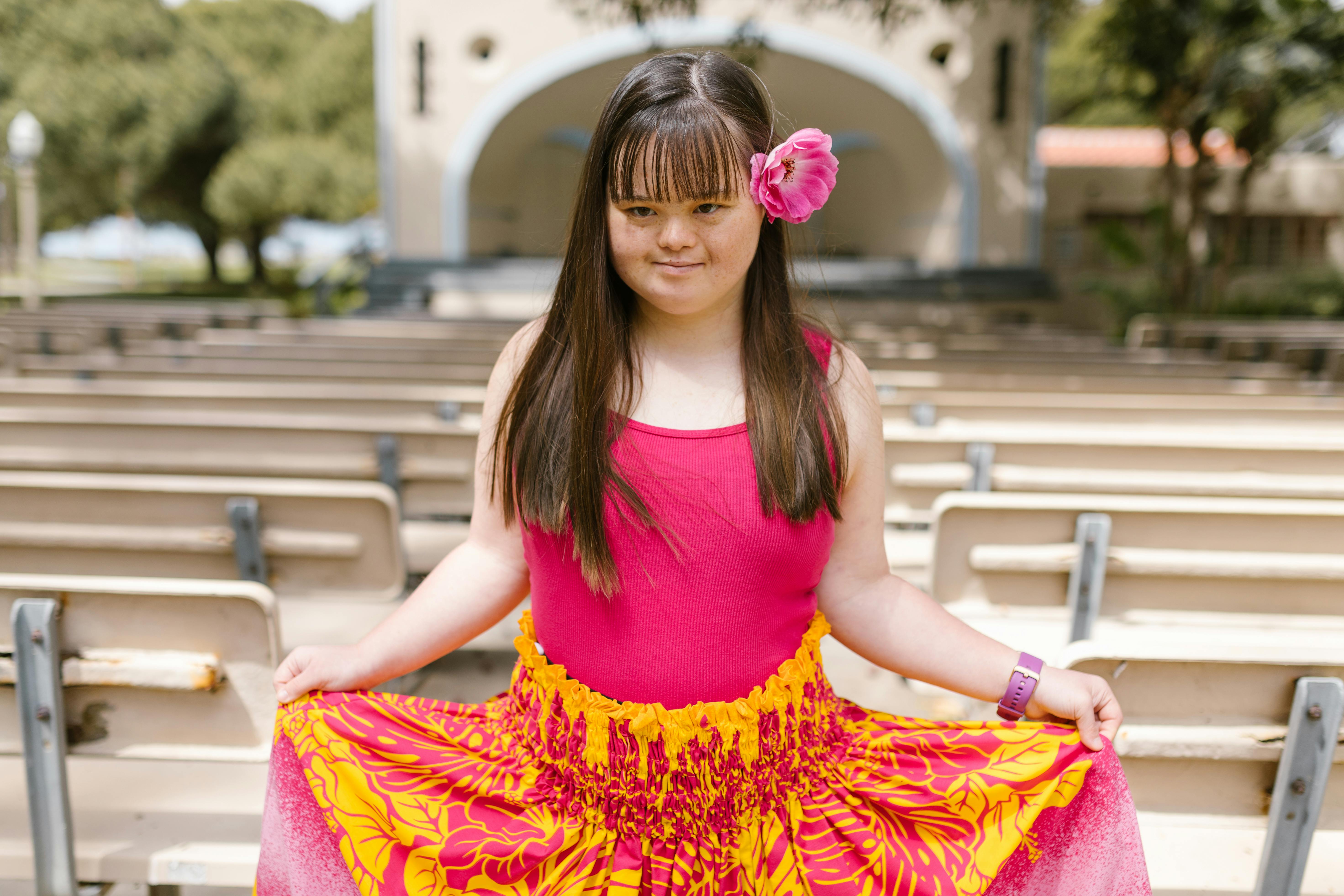 Free Young girl with Down Syndrome posing in a vibrant dress in an outdoor amphitheater. Stock Photo