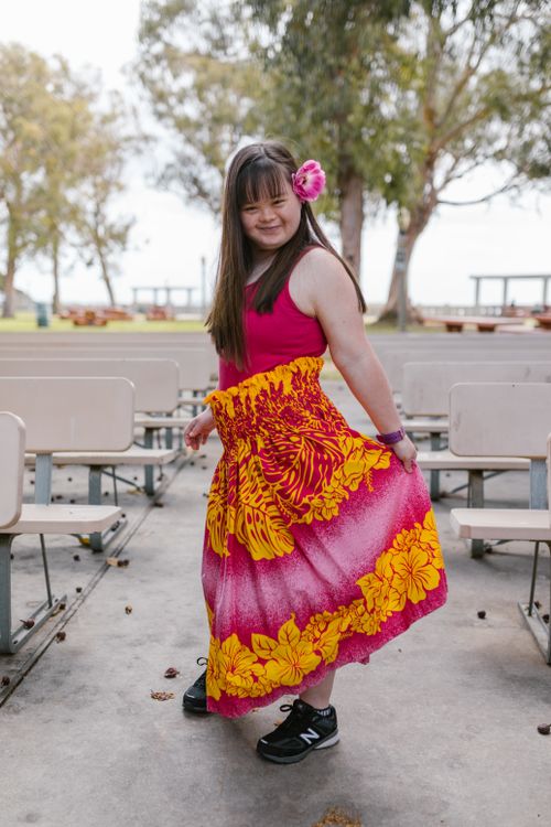 Free A young woman with Down syndrome smiles while posing in a vibrant skirt in a park setting. Stock Photo