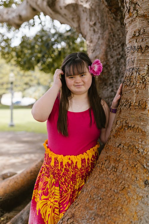 A Girl with a Flower on Her Ear Posing Beside a Tree Trunk