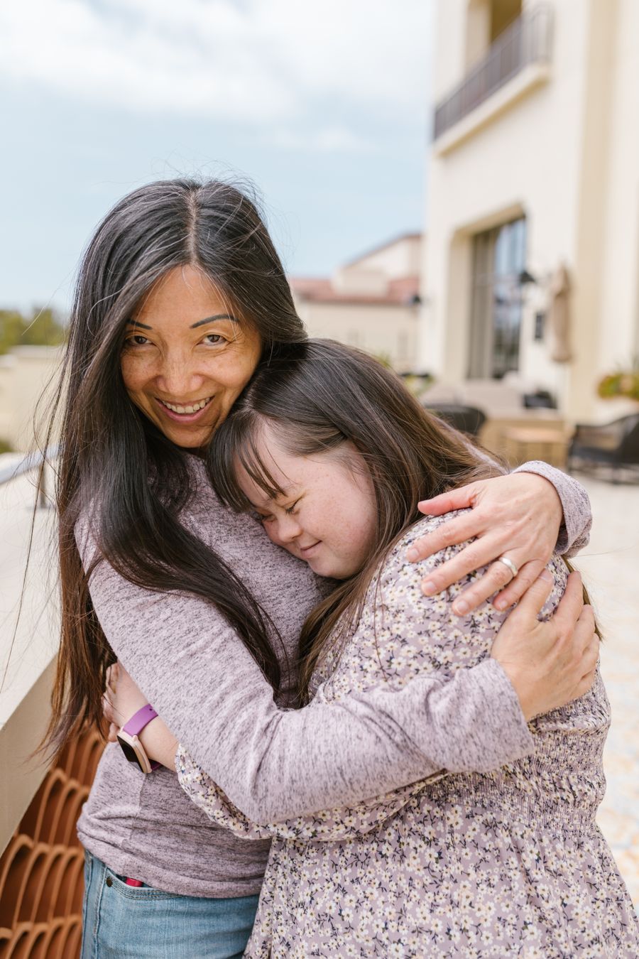 A mother and her adult daughter, who has Down syndrome, share a joyful embrace outdoors.