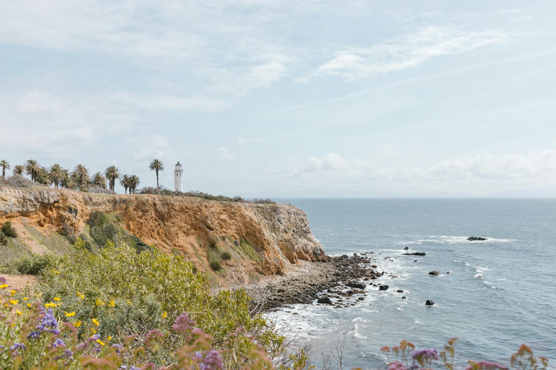 A picturesque view of coastal cliffs with a lighthouse and ocean waves under a sunny sky.
