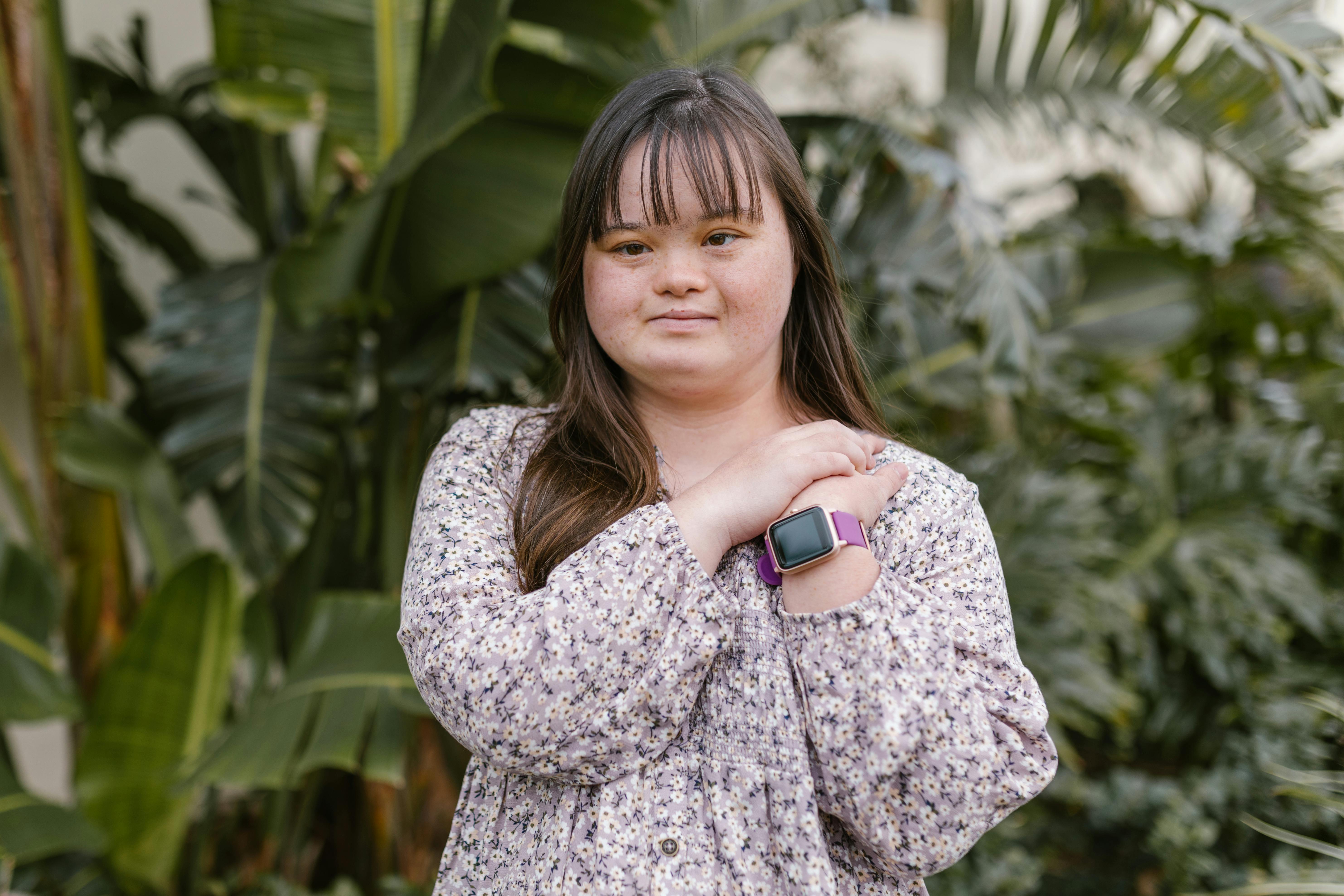 Young woman with down syndrome posing in a floral dress and wristwatch in a lush garden.