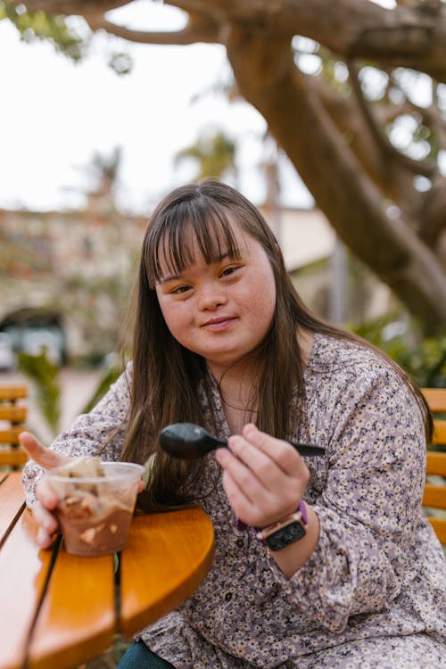 A Girl in a Floral Top Eating a Cup of Pudding