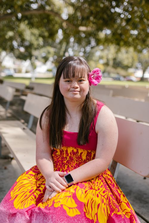 Free A young woman with Down syndrome smiling while sitting on a bench in a colorful dress. Stock Photo