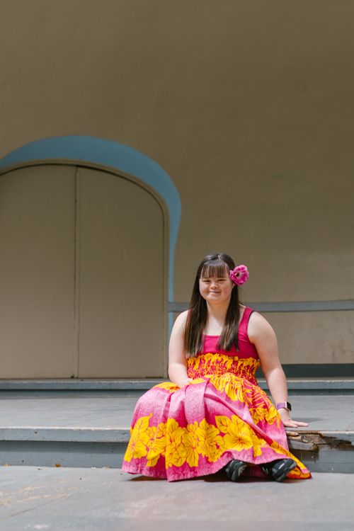 Free A woman with Down syndrome smiles while sitting in a floral dress on a stage. Stock Photo