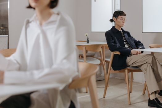 An Asian woman sitting thoughtfully in a modern, minimalist café environment.