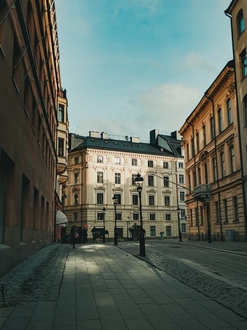 Free A picturesque European street with historic buildings and street lamps under a clear blue sky. Stock Photo