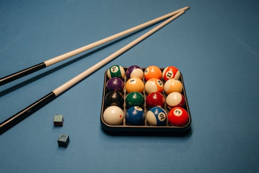 Vibrant billiard balls arranged in a rack on a blue table with cue sticks.
