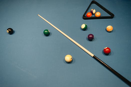 Colorful billiard balls with a cue stick on a blue pool table, ready for a game.