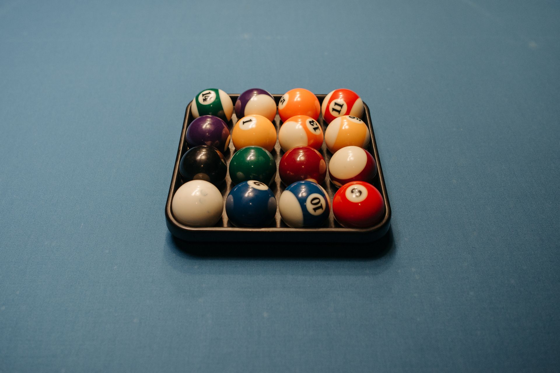 Vibrant billiard balls neatly arranged on a blue pool table in a classic triangular rack.