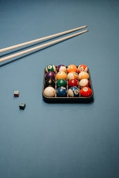 Vibrant billiard ball set with cue sticks on a blue table, perfect for sports enthusiasts.
