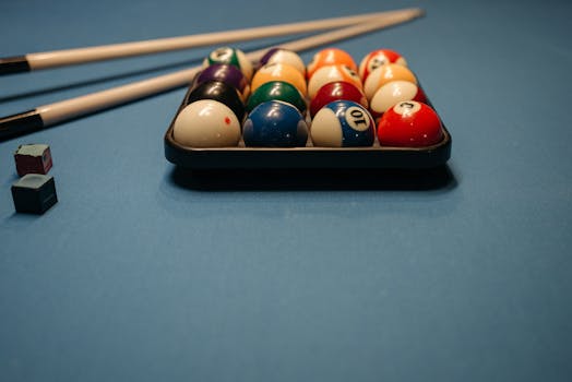 Close-up of arranged billiard balls with cue sticks on a blue pool table, perfect for game enthusiasts.