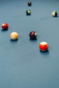 Colorful billiard balls scattered on a blue pool table during a game indoors.