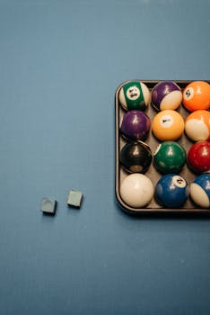 Colorful billiard balls neatly arranged on a blue pool table with cue chalk.