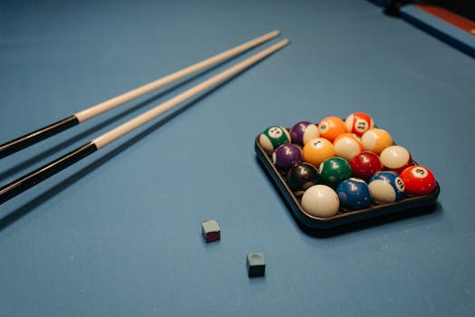 Arrangement of billiard balls and cue sticks on a blue table, perfect for sports enthusiasts.