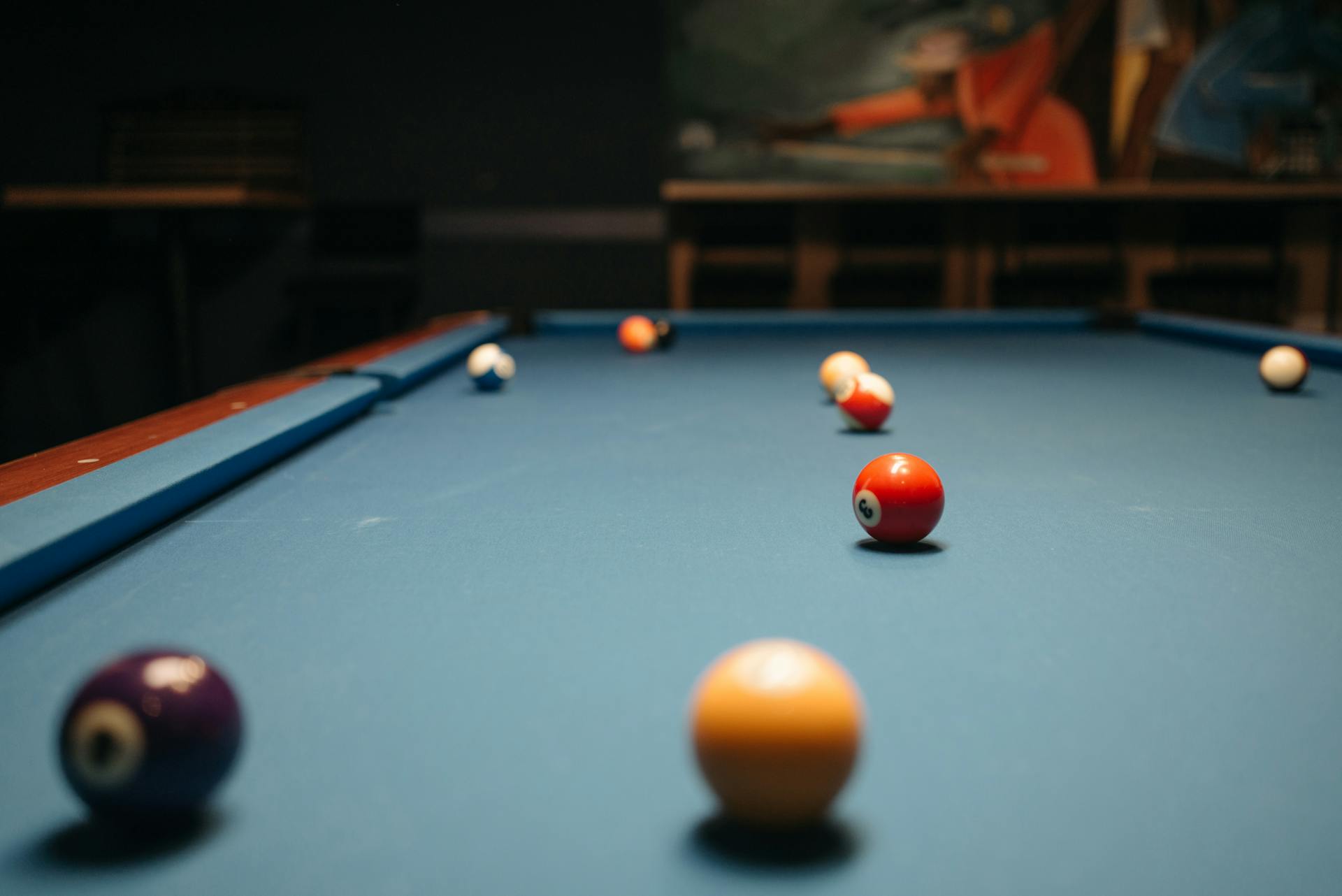 Colorful billiard balls on a pool table in a dimly lit room, showcasing depth and focus.