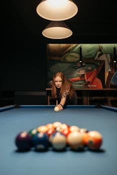 Woman focusing on a cue ball shot on a vibrant billiard table in a stylish pool hall.