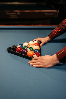 Close-up of hands setting up colorful billiard balls on a table. Perfect for game enthusiasts.