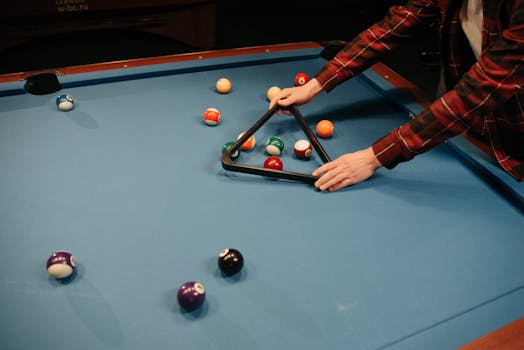 A person arranging billiard balls on a blue pool table in preparation for a game indoors.